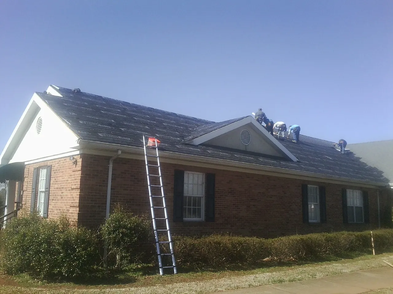 Crew tearing shingles off a brick ranch roof with a ladder set — Emergency Roof Repair work by our crew in Louisa
