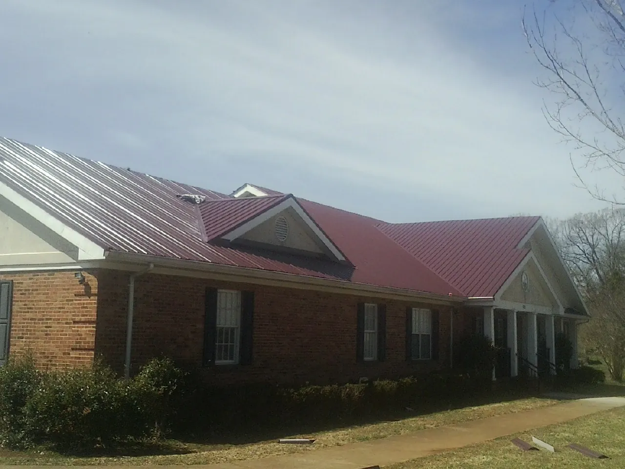 Red metal roof with gabled entries on a long brick building, from a Hail Damage Roof Repair job in Louisa