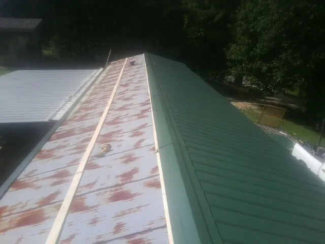 Old rusted panels beside newly installed green metal roofing — Wind Damage Roof Repair by Roofing Brothers in Louisa