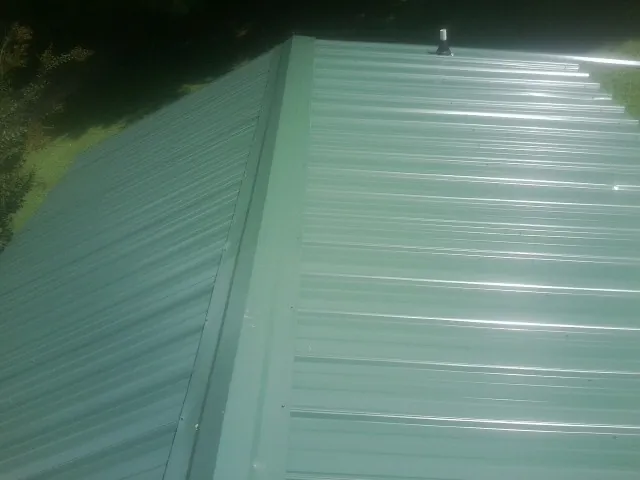 New green metal panels meeting at the ridge of a roof — Flat Roof Repair work by our crew in Louisa