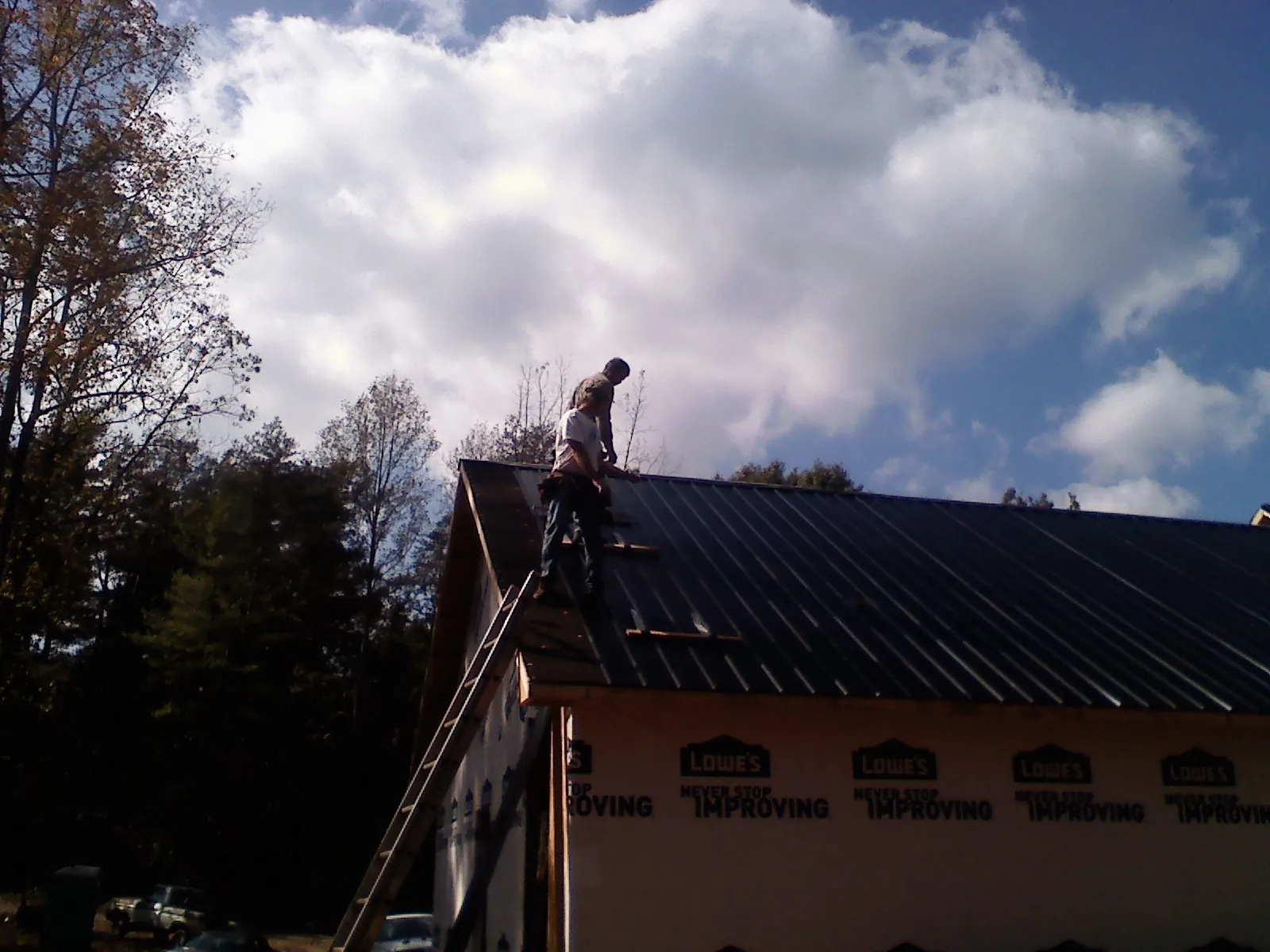 Roofer fastening dark metal panels high against a cloudy sky, from a Roof Inspection job in Louisa