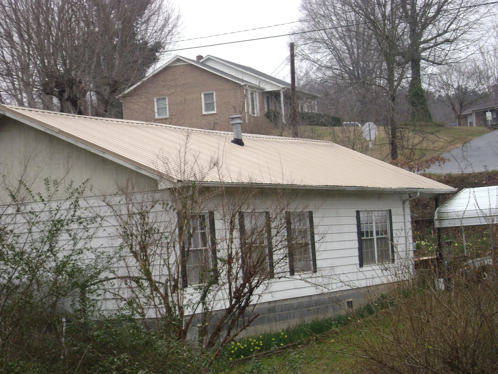 Tan metal roof on a white sided house set into a hillside — Commercial Roofing by Roofing Brothers in Louisa