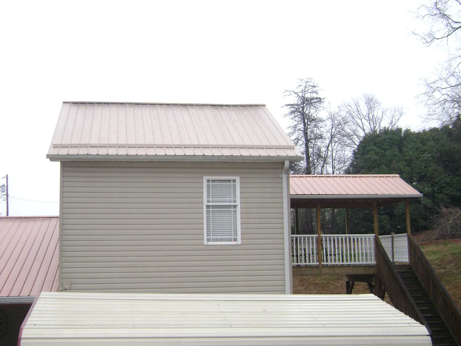 Tan metal roofs on a two story addition and attached porch, from a Roof Replacement job in Louisa